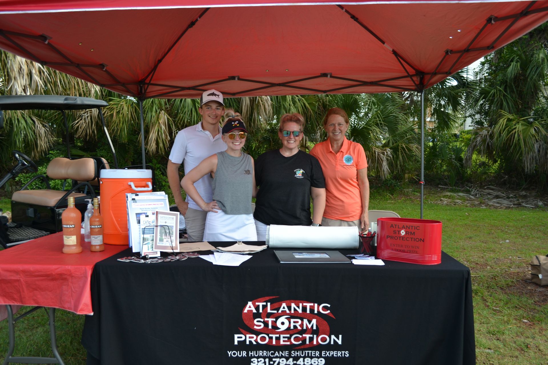 Four people at an Atlantic Storm Protection booth under a red canopy outdoors