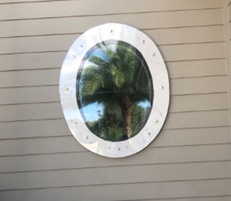 Oval porthole-style window in a beige wall reflecting palm trees and blue sky