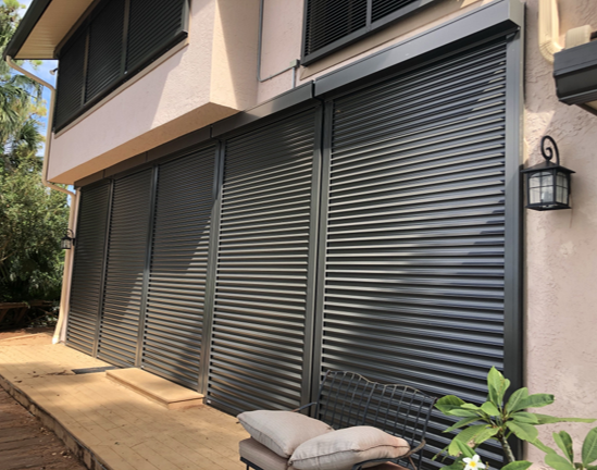 Closed gray window shutters on a house exterior with a wall lantern and potted plant.