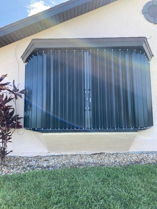 House exterior with a large window covered by dark vertical blinds and a small lawn in front