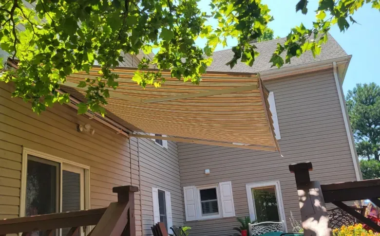 Backyard patio with beige house, striped awning, and leafy tree branches overhead