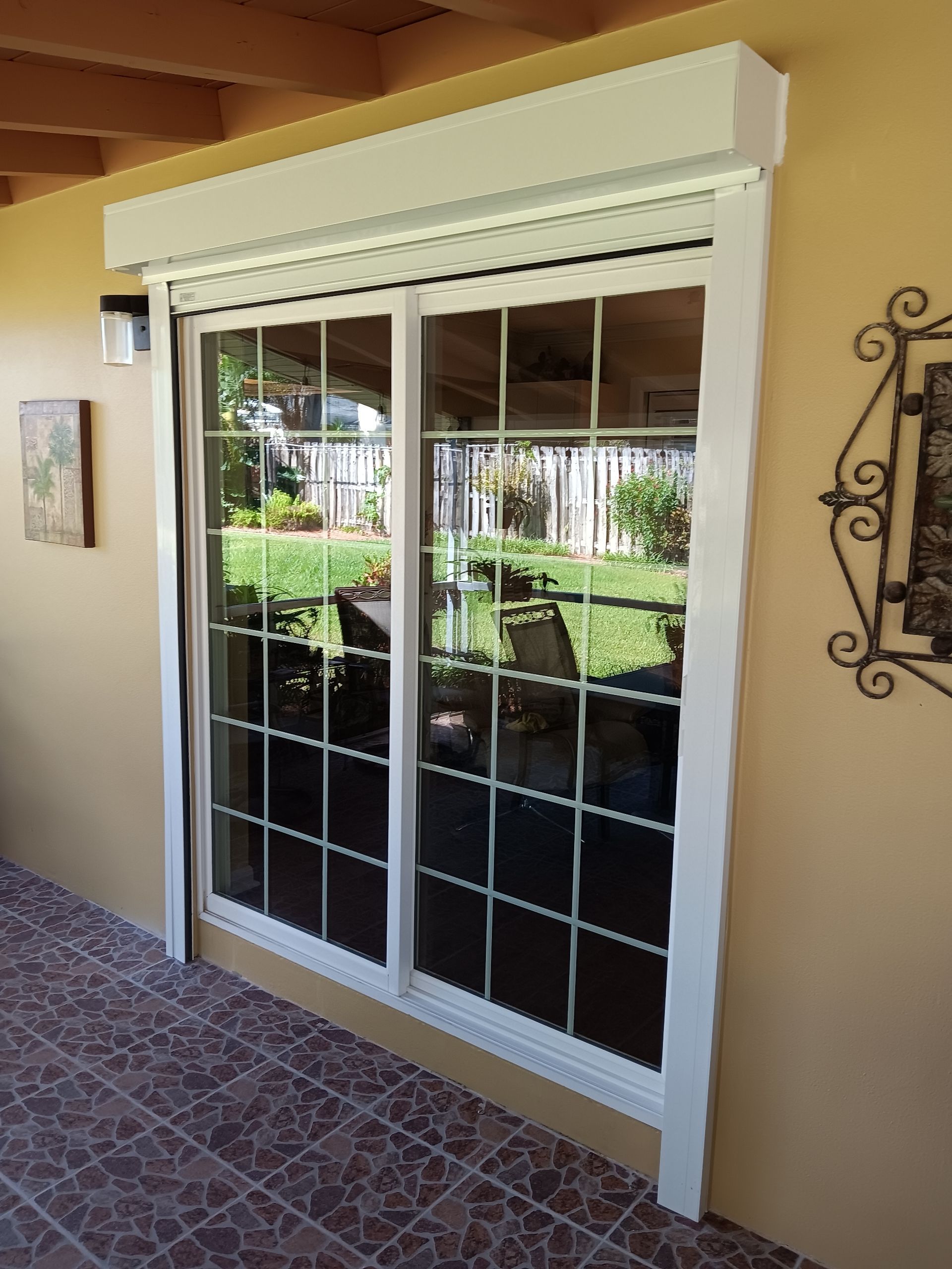 White sliding glass patio door with decorative grid and awning, reflecting a garden outside
