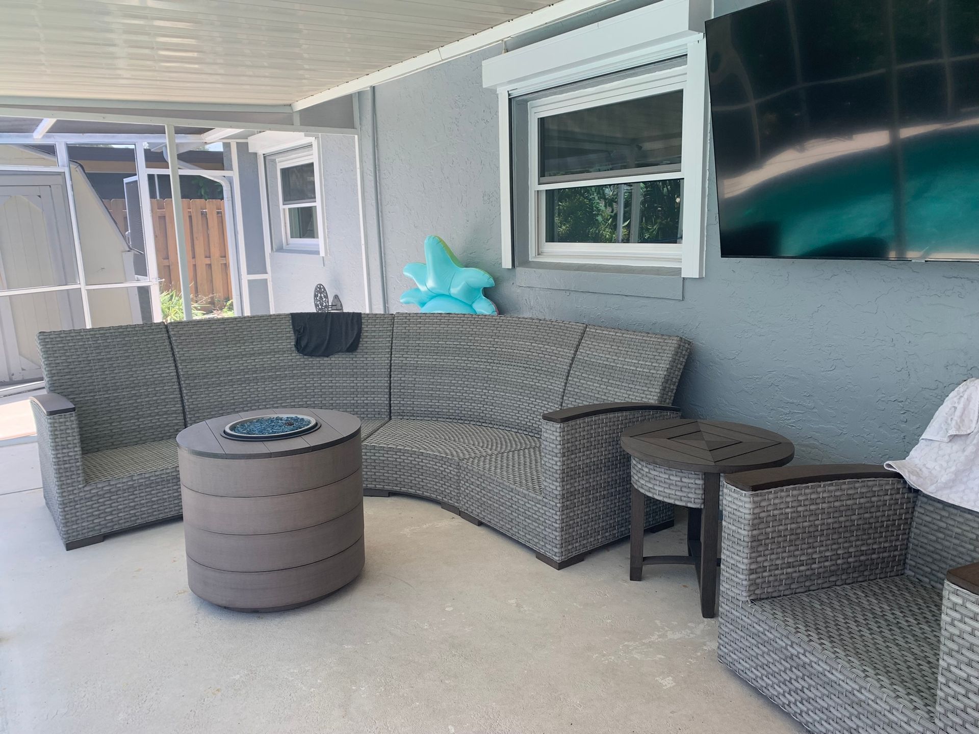 Covered patio seating area with gray sectional sofas, round coffee table, and wall-mounted TV