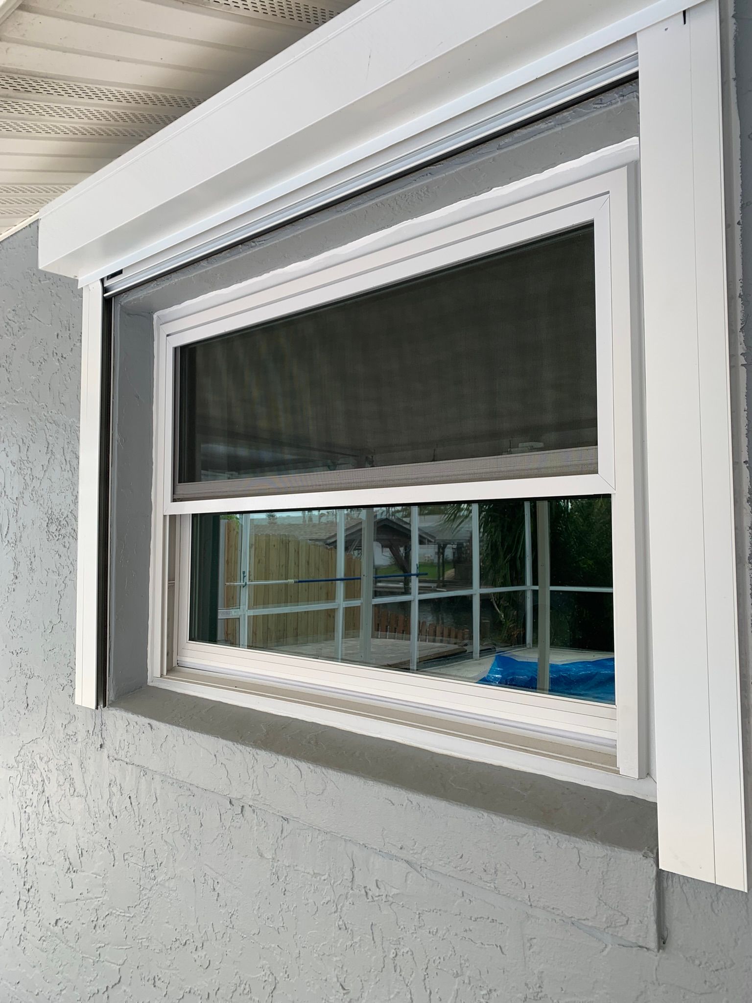 Open window with white frame and dark screen, showing a house exterior and backyard view.