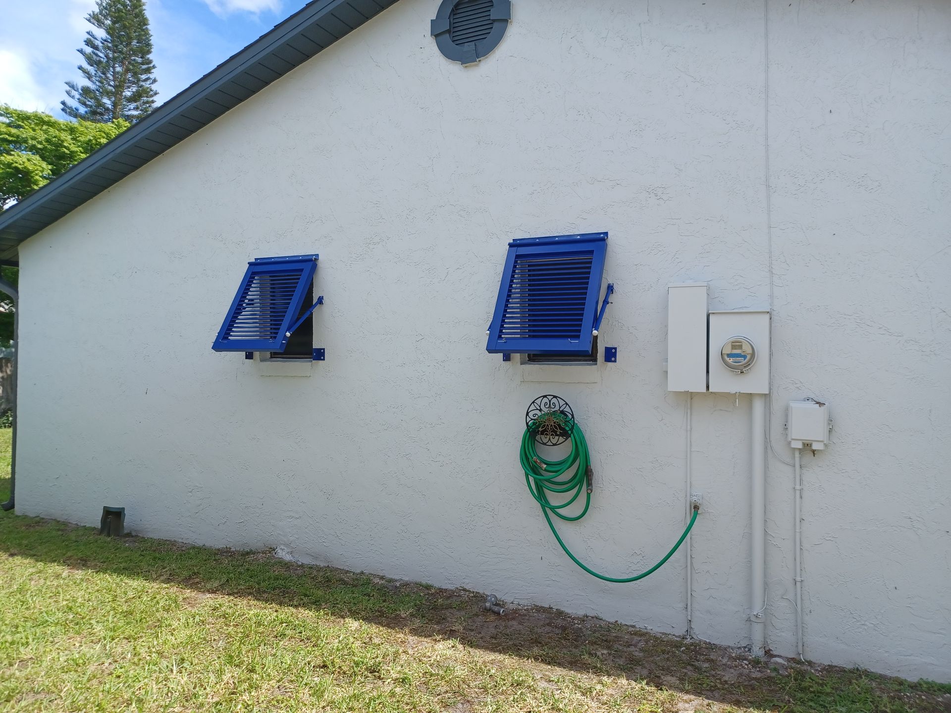 White building wall with two blue vents and a coiled green hose beside electrical boxes