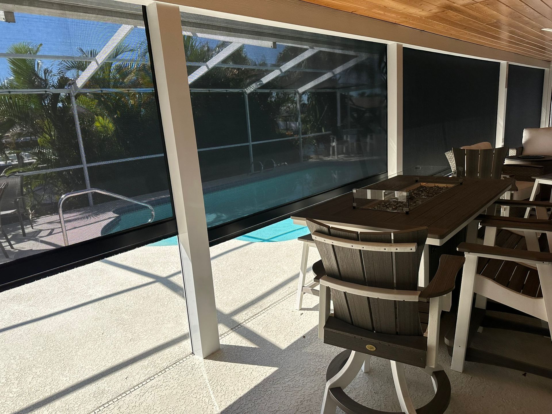 Covered patio with dining table and chairs beside a screened pool area