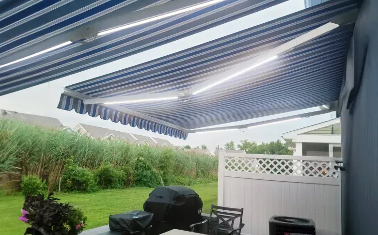 Striped retractable awning over a patio with outdoor seating and grill beside a green yard