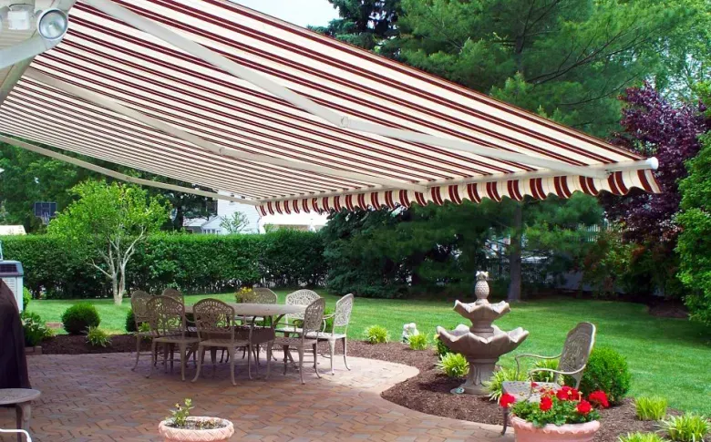 Patio with red-and-white striped awning, outdoor table and chairs, fountain, and lush garden greenery