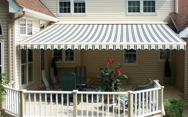Covered patio with striped awning, white railing, and potted flowers outside a house