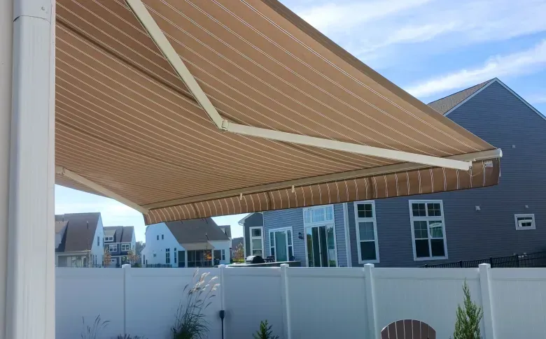 Striped tan patio awning extending over a fenced backyard with modern homes in the background