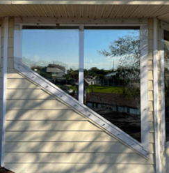 Diagonal-trimmed window on a beige house reflecting trees and a yard outdoors