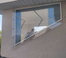 Tilted glass awning window on a beige stucco building wall with blue sky reflections