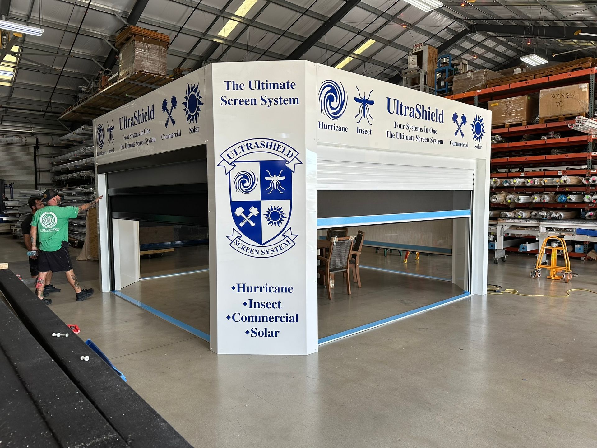 White portable event booth in a warehouse, with blue signage and logos on four sides.