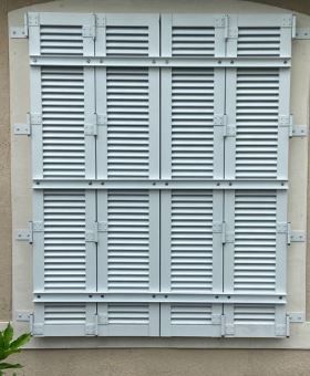 Closed white louvered shutters on a beige exterior wall