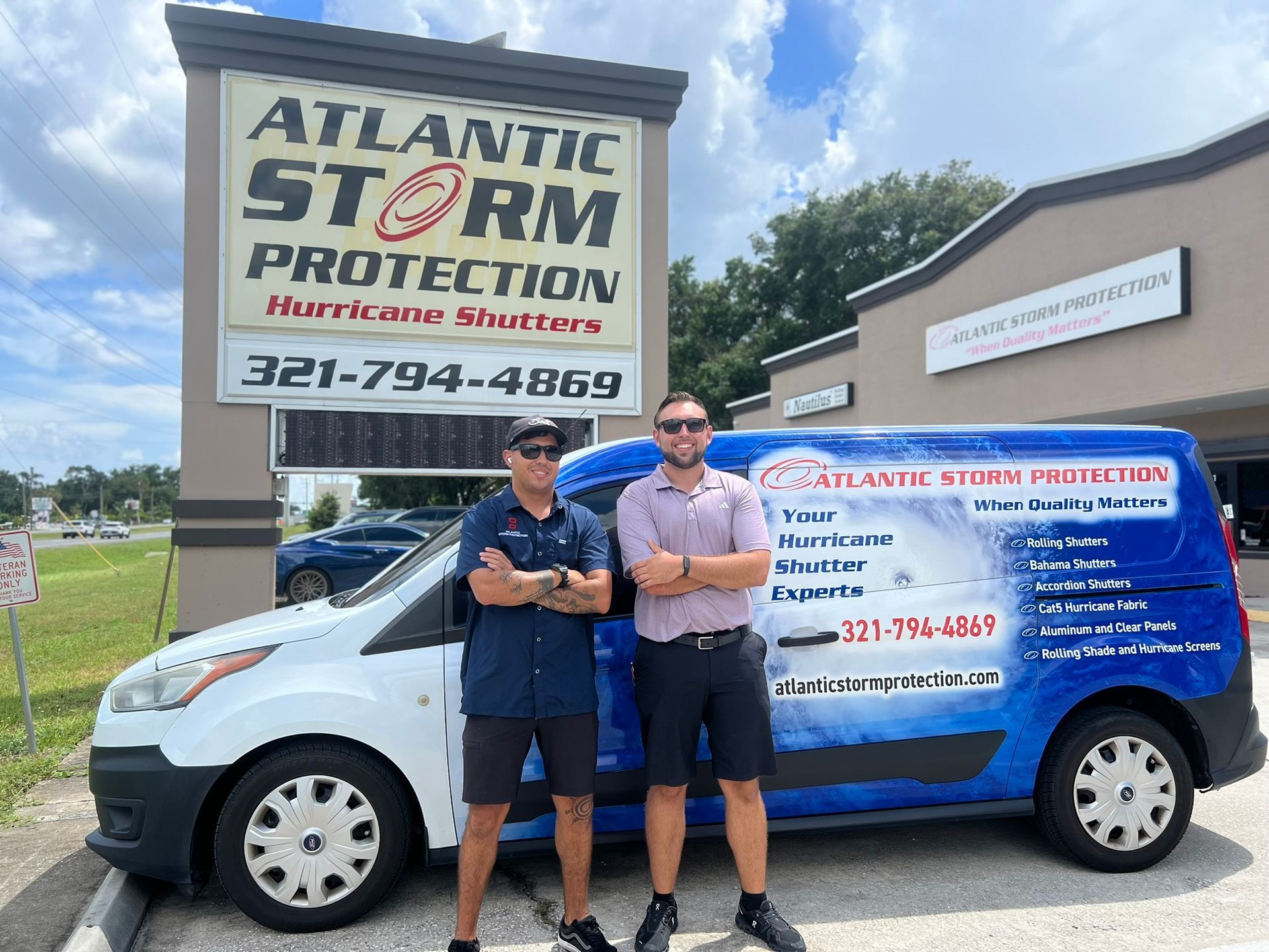 Two men stand beside a white service van with a blue storm protection ad outside Atlantic Storm Protection.