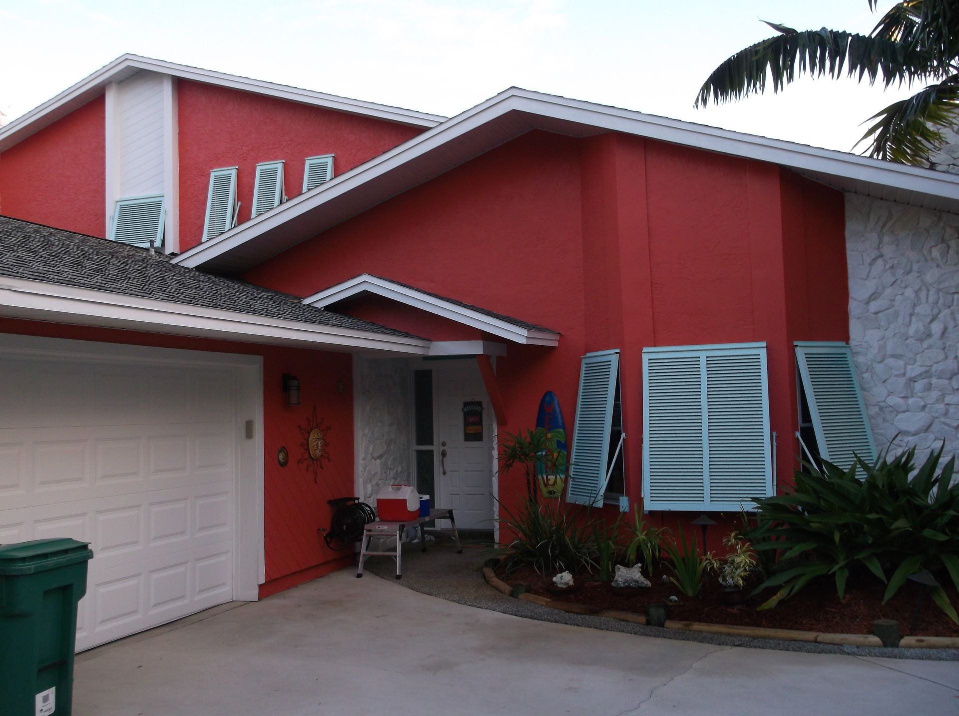 Red stucco house exterior with white garage door, front entry, and tropical plants.