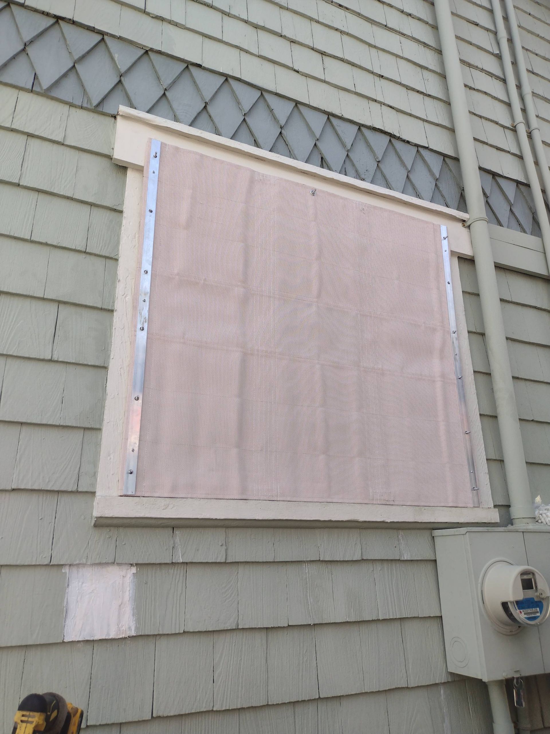 Window covered with pink insulation board on gray shingled house exterior