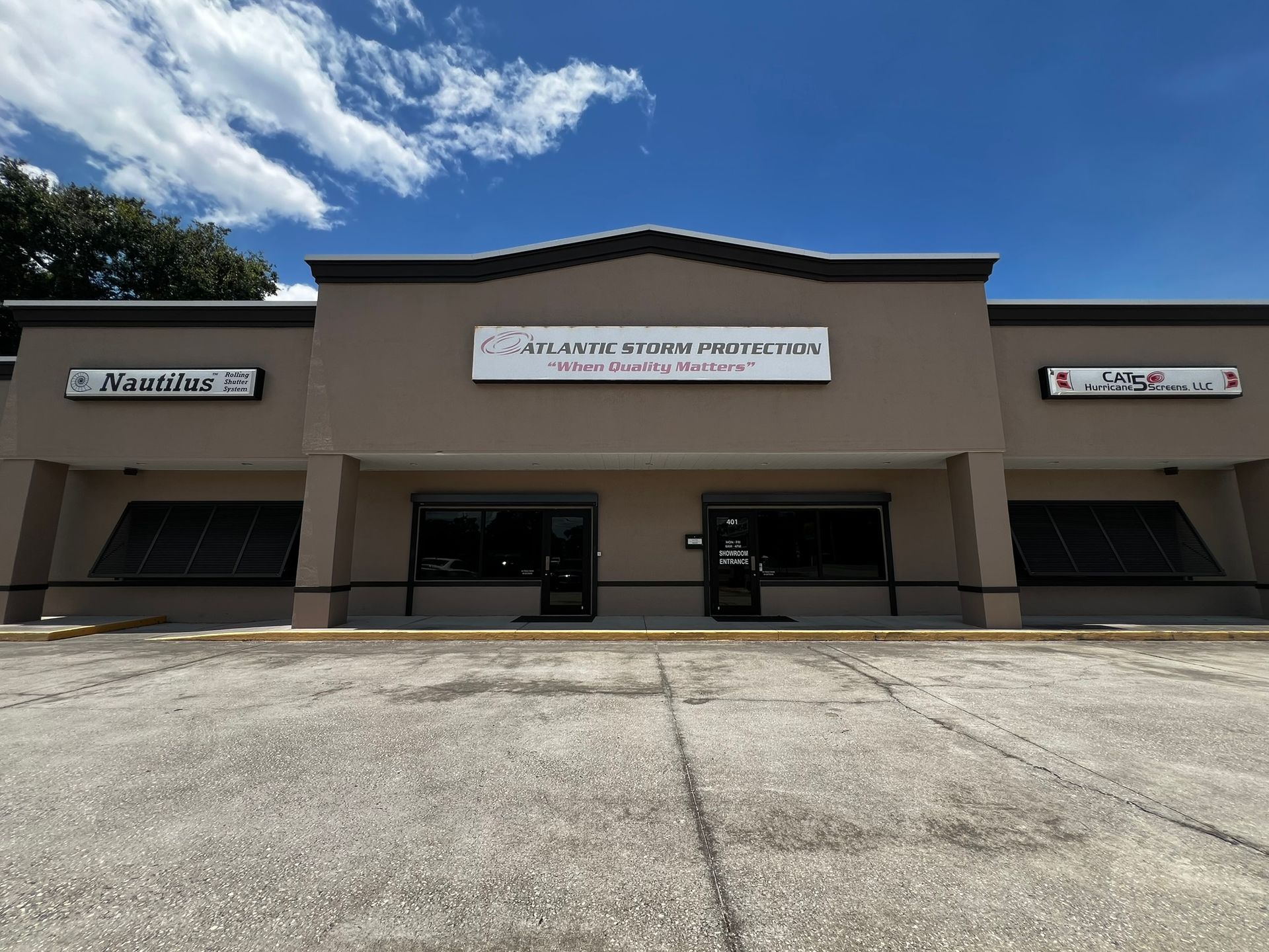 Exterior of a beige storefront with a central sign and empty parking lot under a blue sky