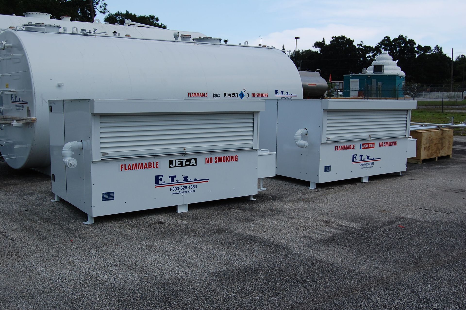 White industrial tanks and equipment units on gravel in an outdoor yard.