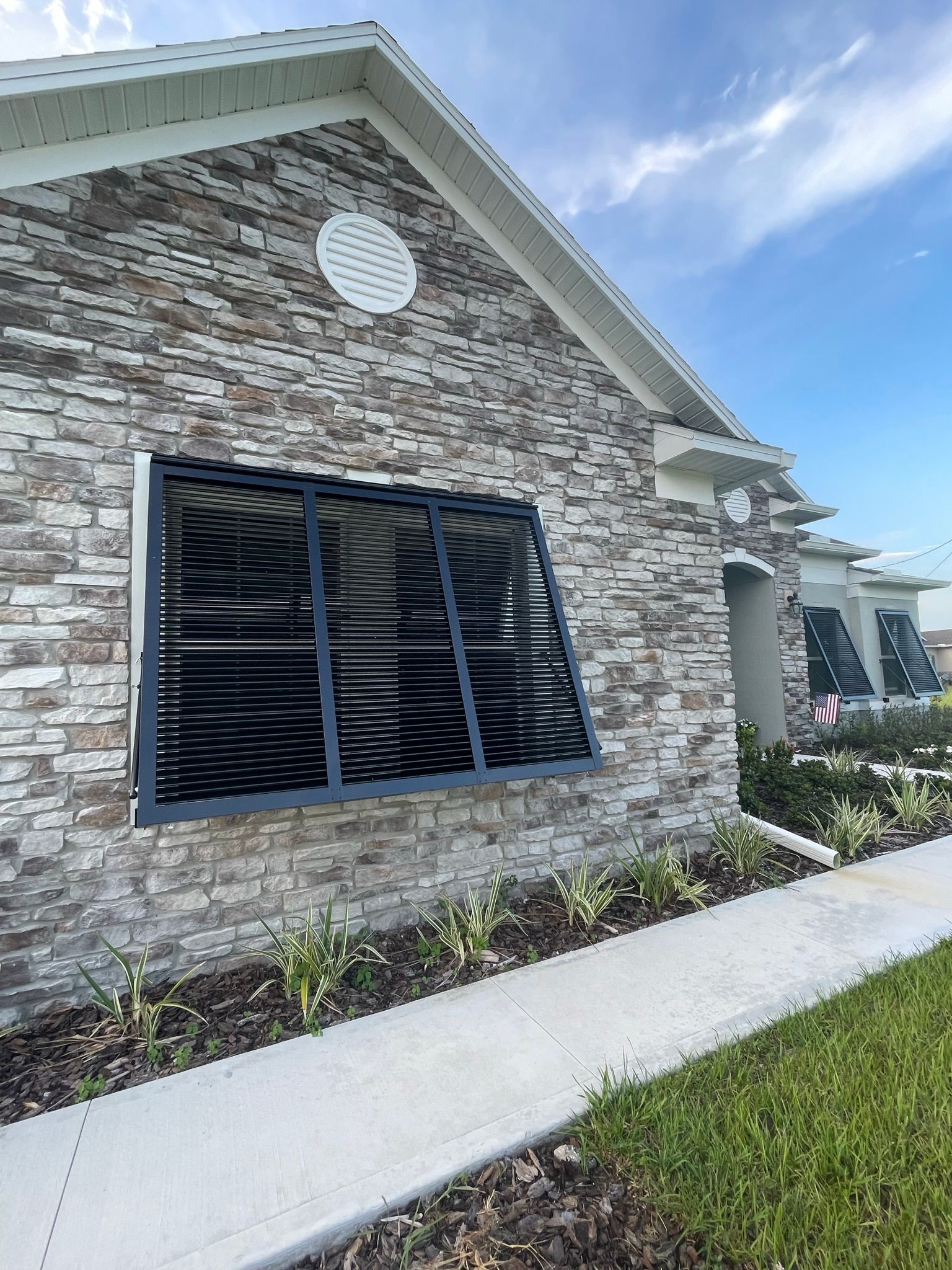 Brick house exterior with broken black window shutters and white trim along a sidewalk