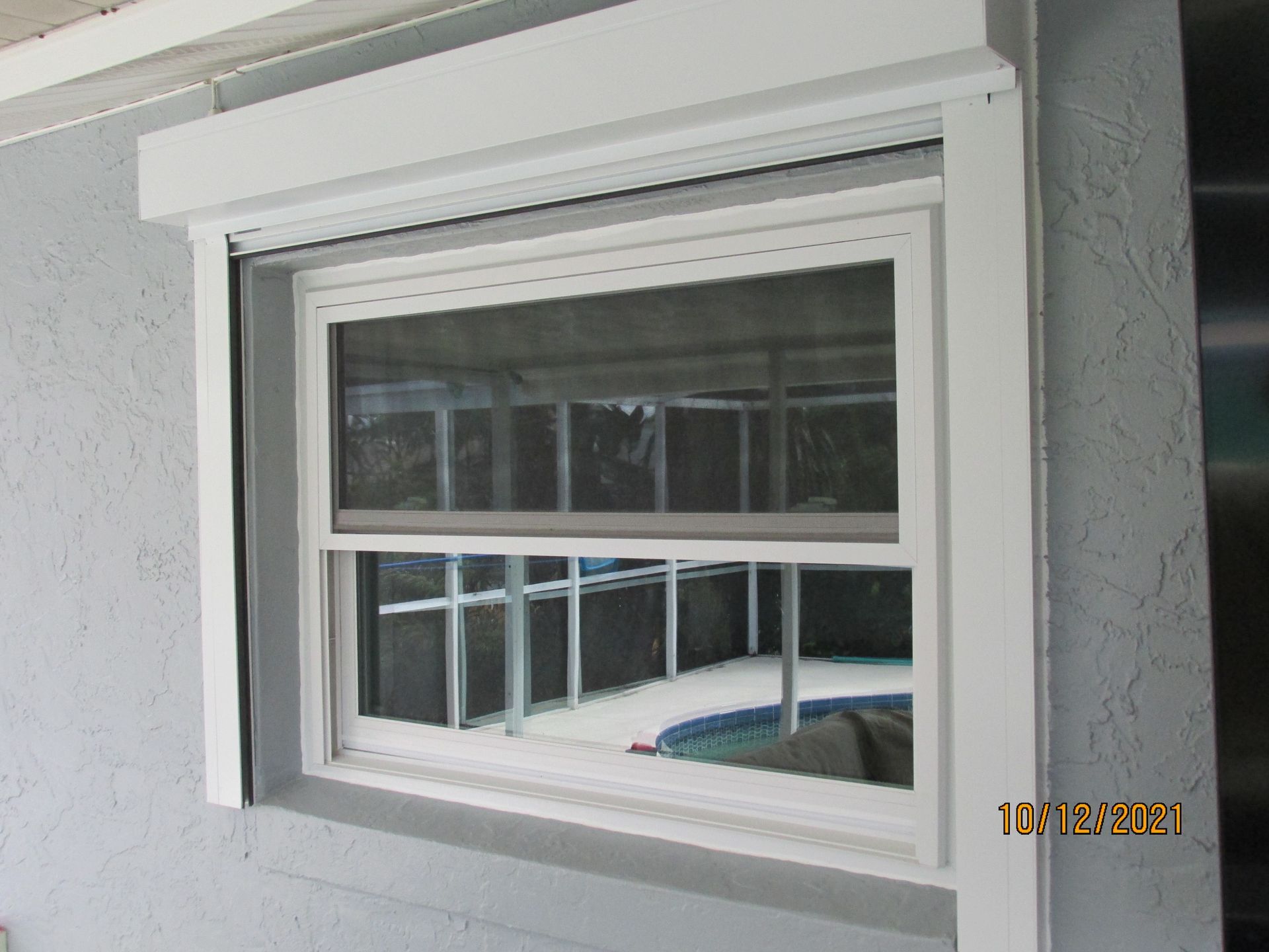White-framed window with a small awning, viewed from outside a stucco wall.
