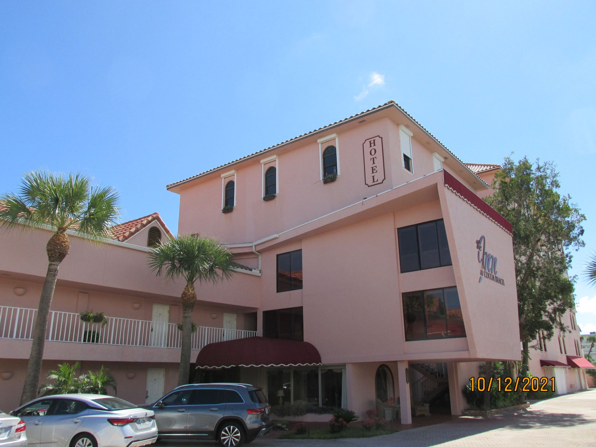 Pink apartment building with palm trees and parked cars under a clear blue sky