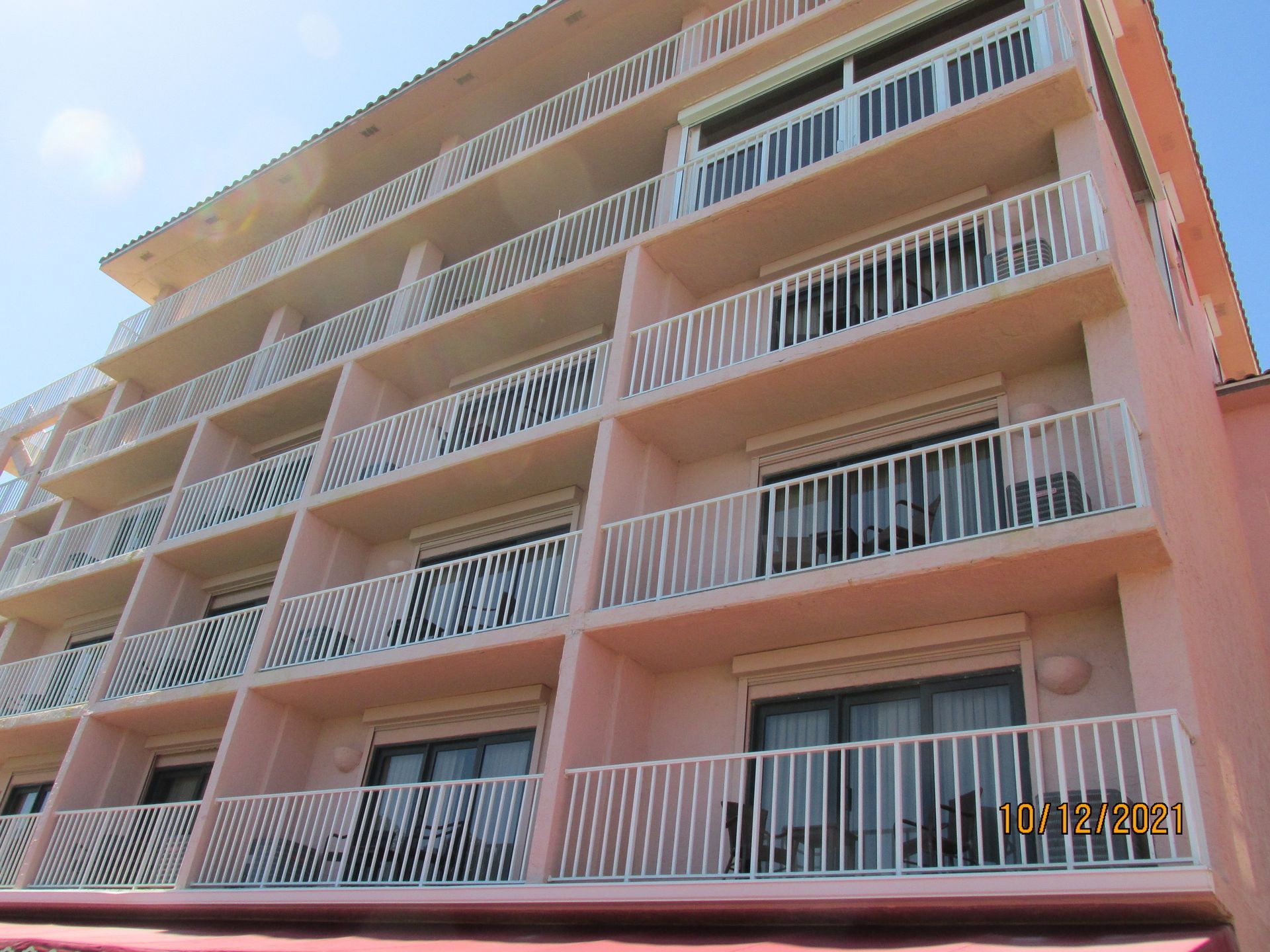 Low-rise peach apartment building with stacked balconies and white railings under a clear sky