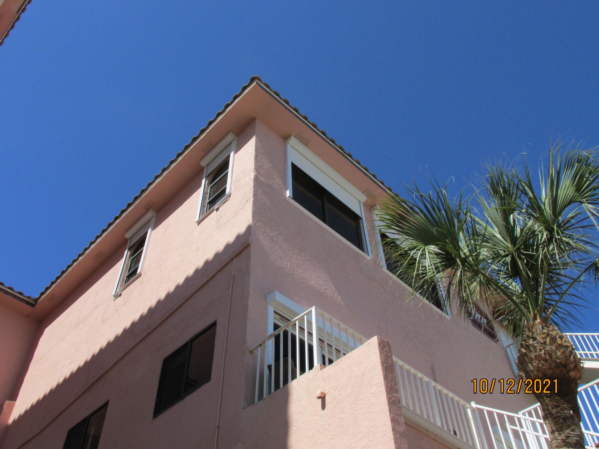 Pink building with balconies and palm tree against a blue sky