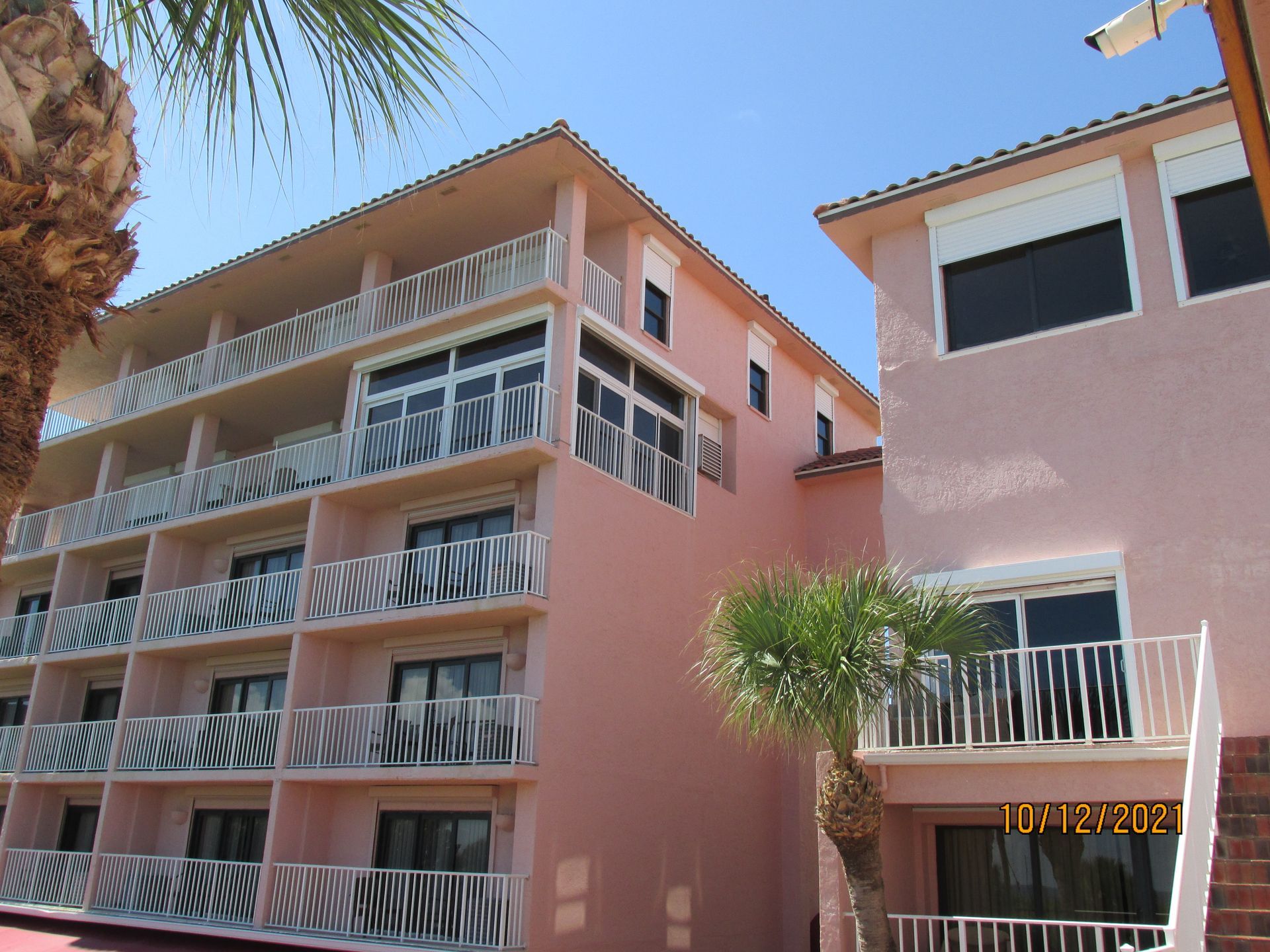 Pink apartment building with balconies and palm trees under a clear blue sky