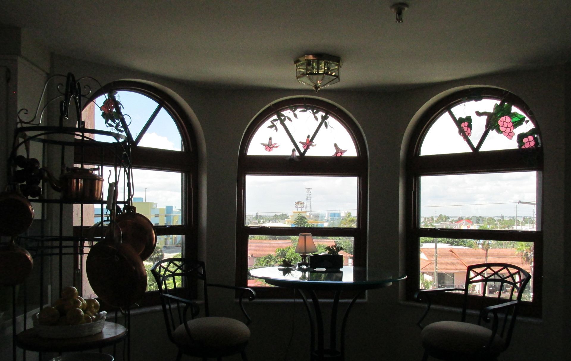 Dim cafe interior with three arched windows, tables, and chairs silhouetted against daylight.