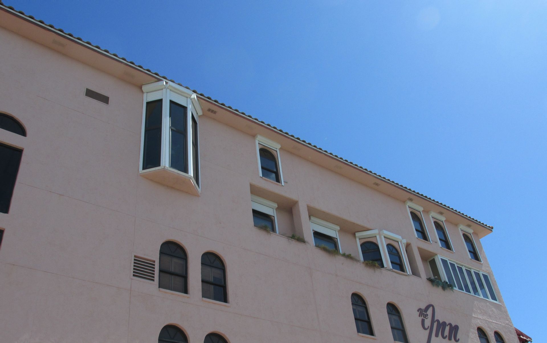 Pink stucco building with arched windows against a bright blue sky