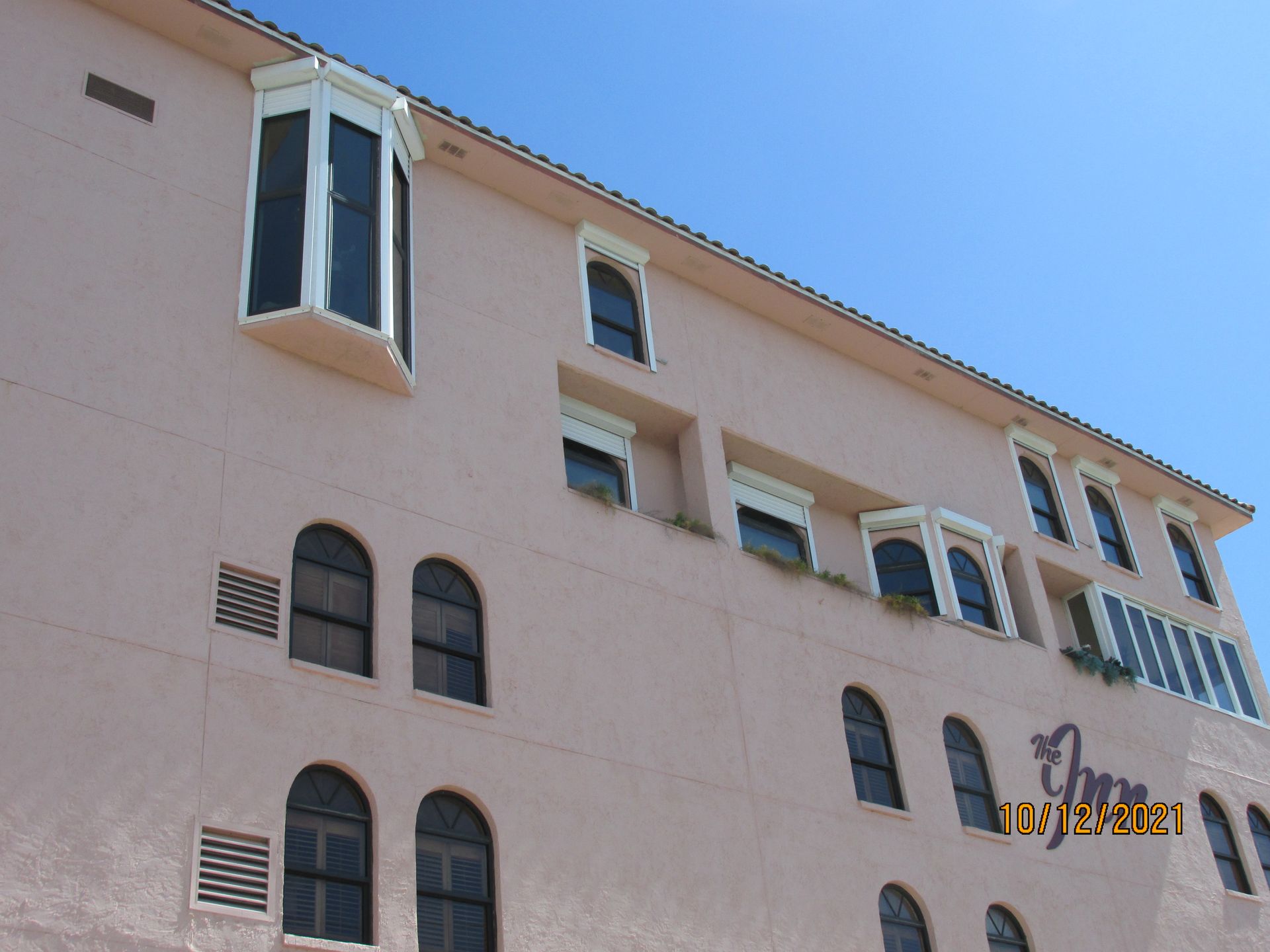 Pink stucco apartment building with arched windows under a clear blue sky
