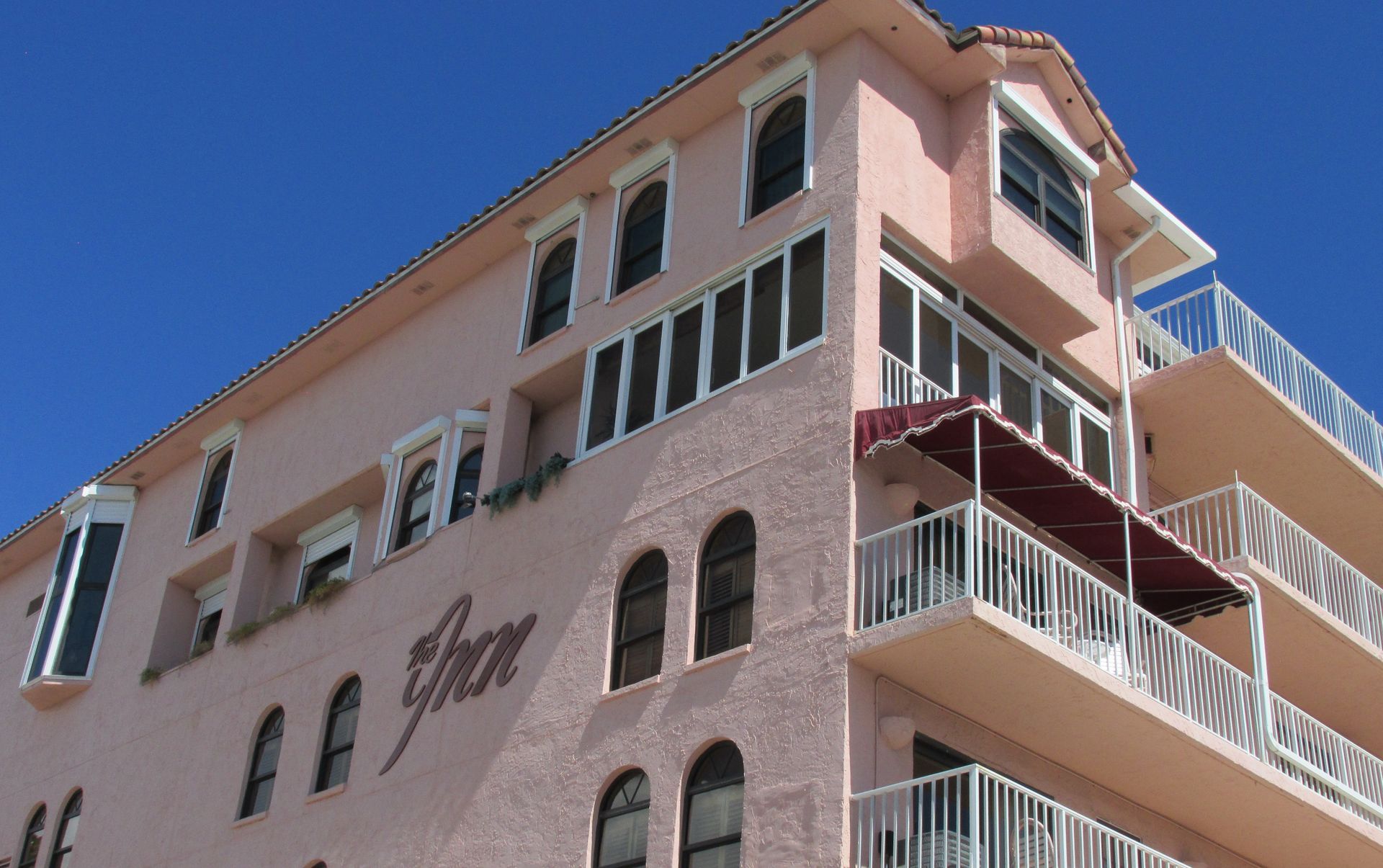 Pink stucco apartment building with balconies and arched windows against a blue sky