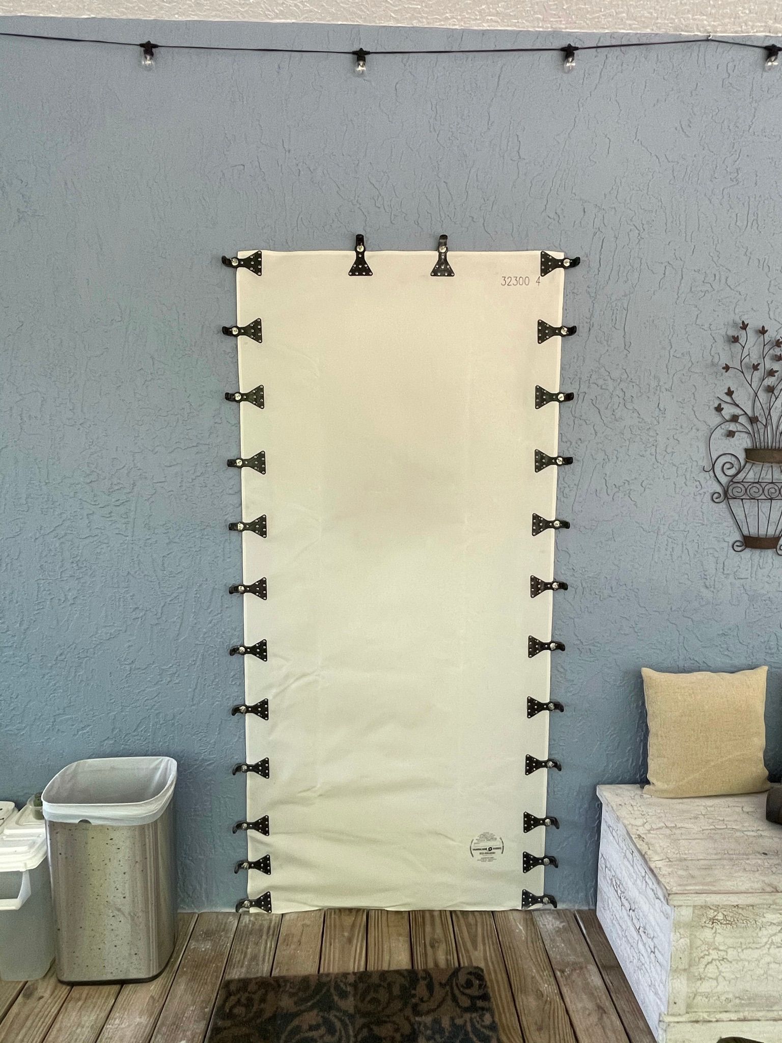 White hanging tarp or sheet with black clips on a gray wall, above a wooden floor in an industrial space