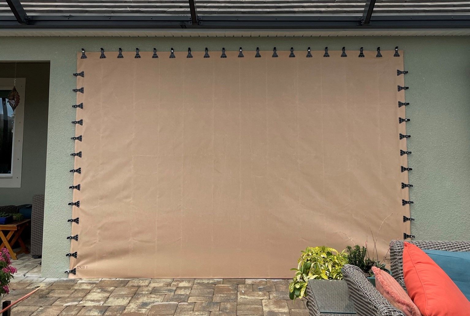 Large beige privacy screen or tarp hanging on a patio wall, with outdoor furniture at the edges.