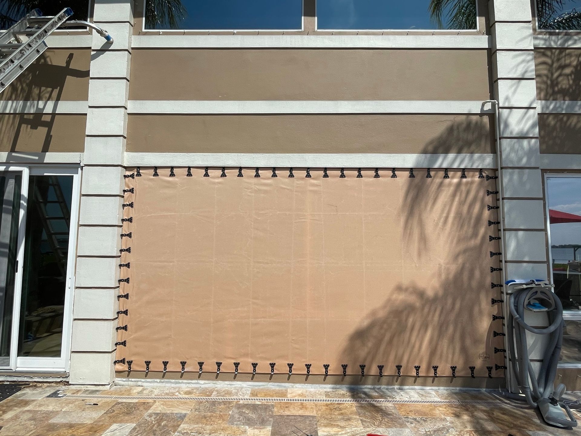 Closed tan storefront shutter on a beige building with white trim and windows above