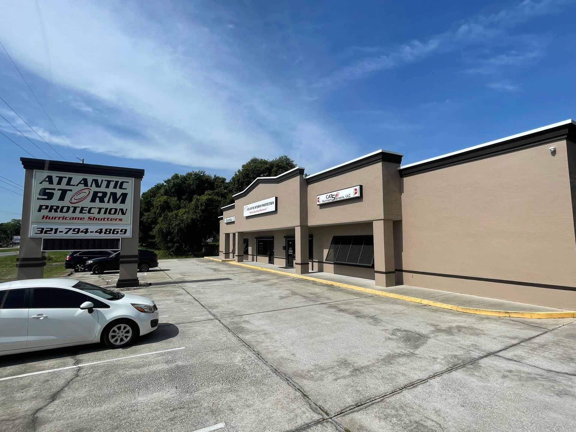 Strip mall storefronts under a blue sky, with a sign for Atlantic Self Storage and a parked white car.