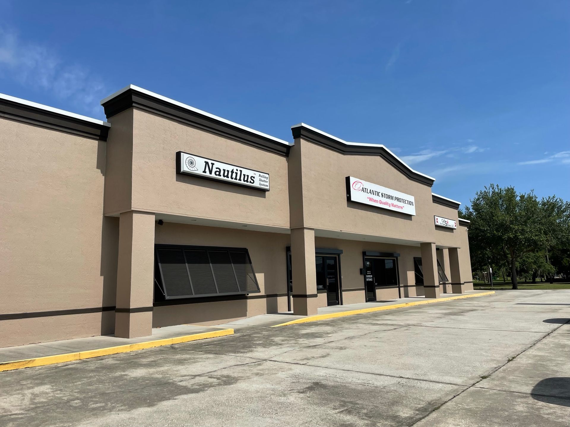 Strip mall storefronts with tan stucco walls, parked lot, and blue sky on a sunny day