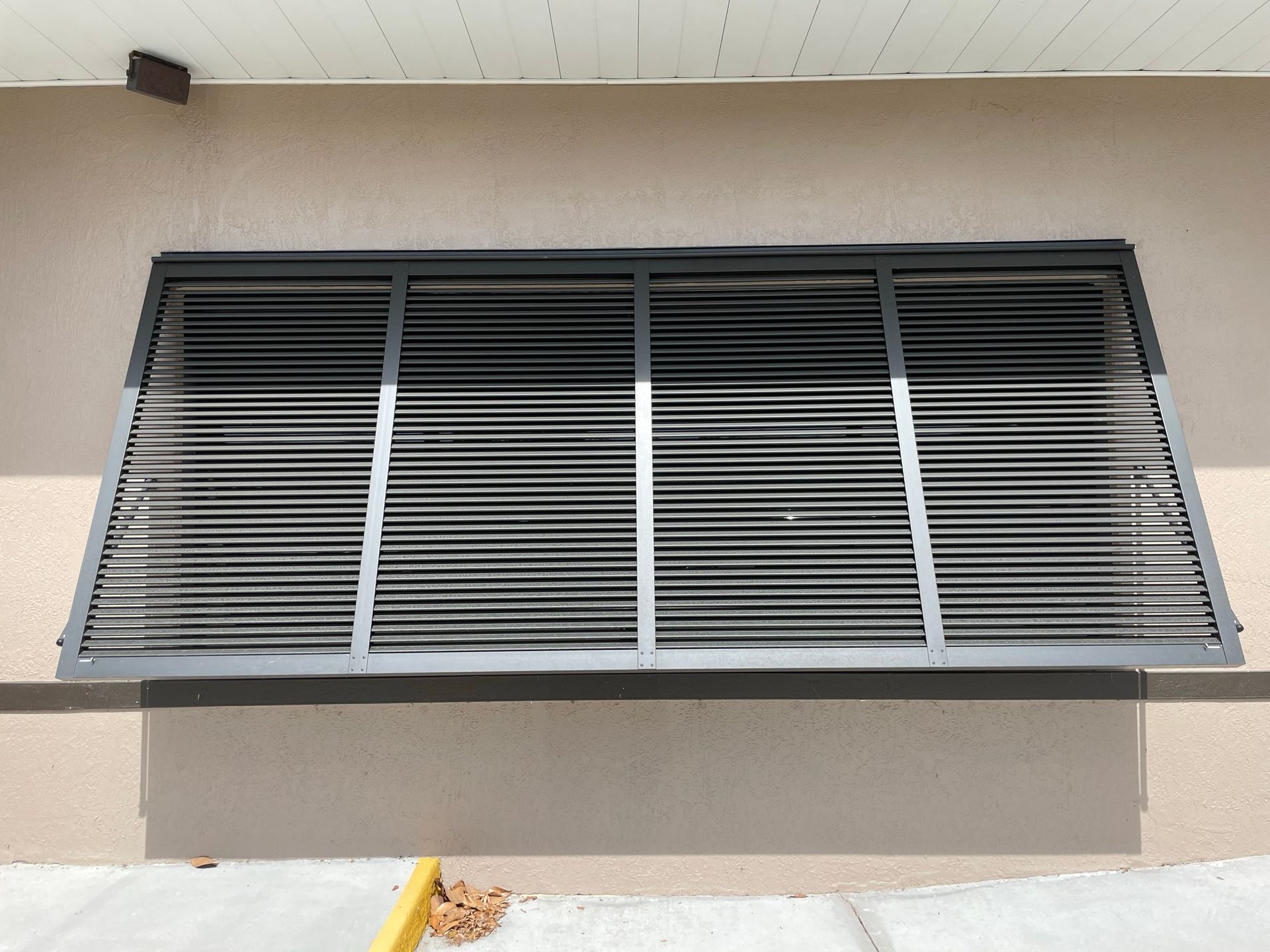 Gray metal window shutters on a beige building exterior, angled open above a ledge.