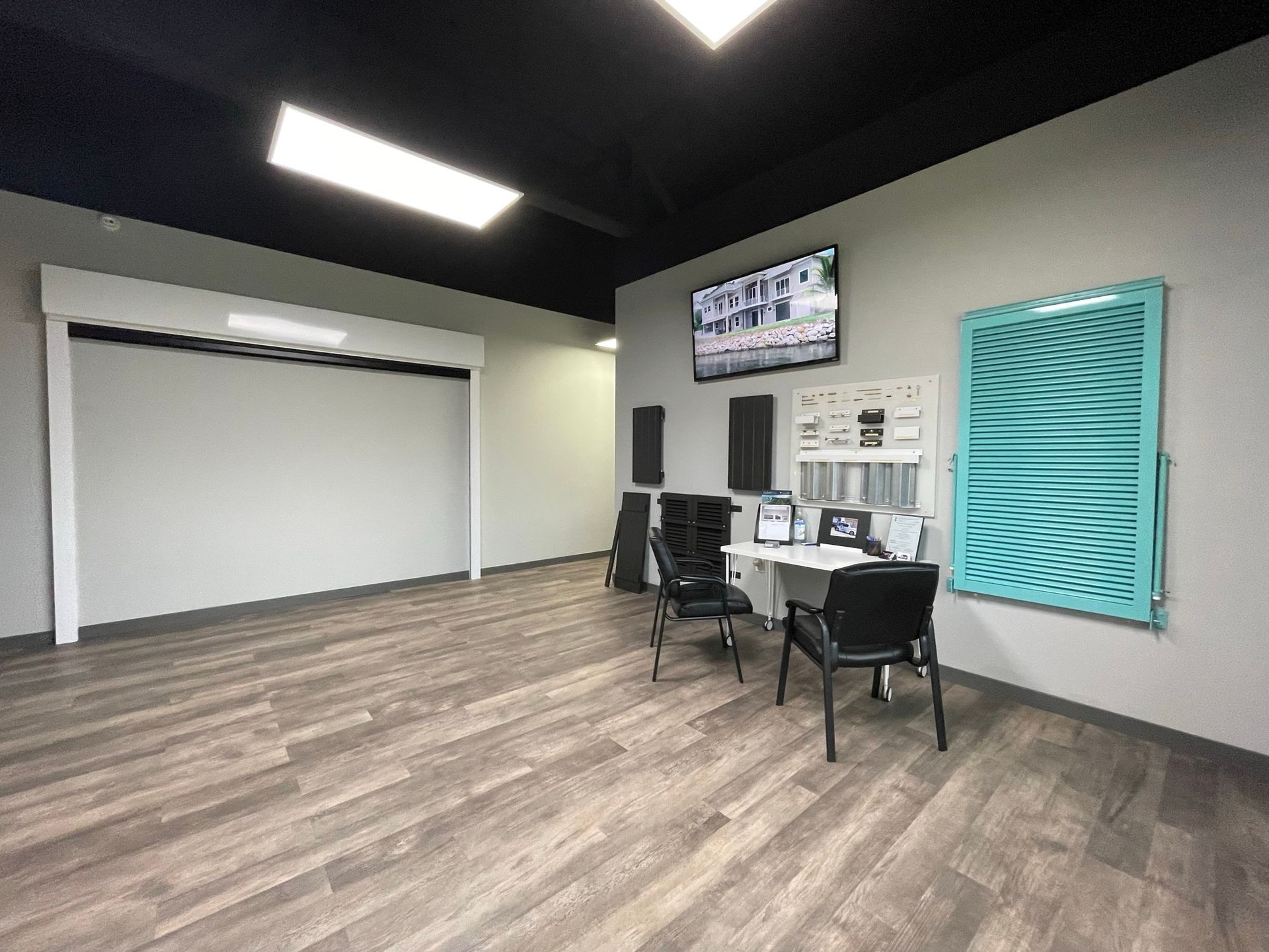 Modern meeting room with chairs, small desks, wall-mounted TV, and large whiteboard on a wood floor.