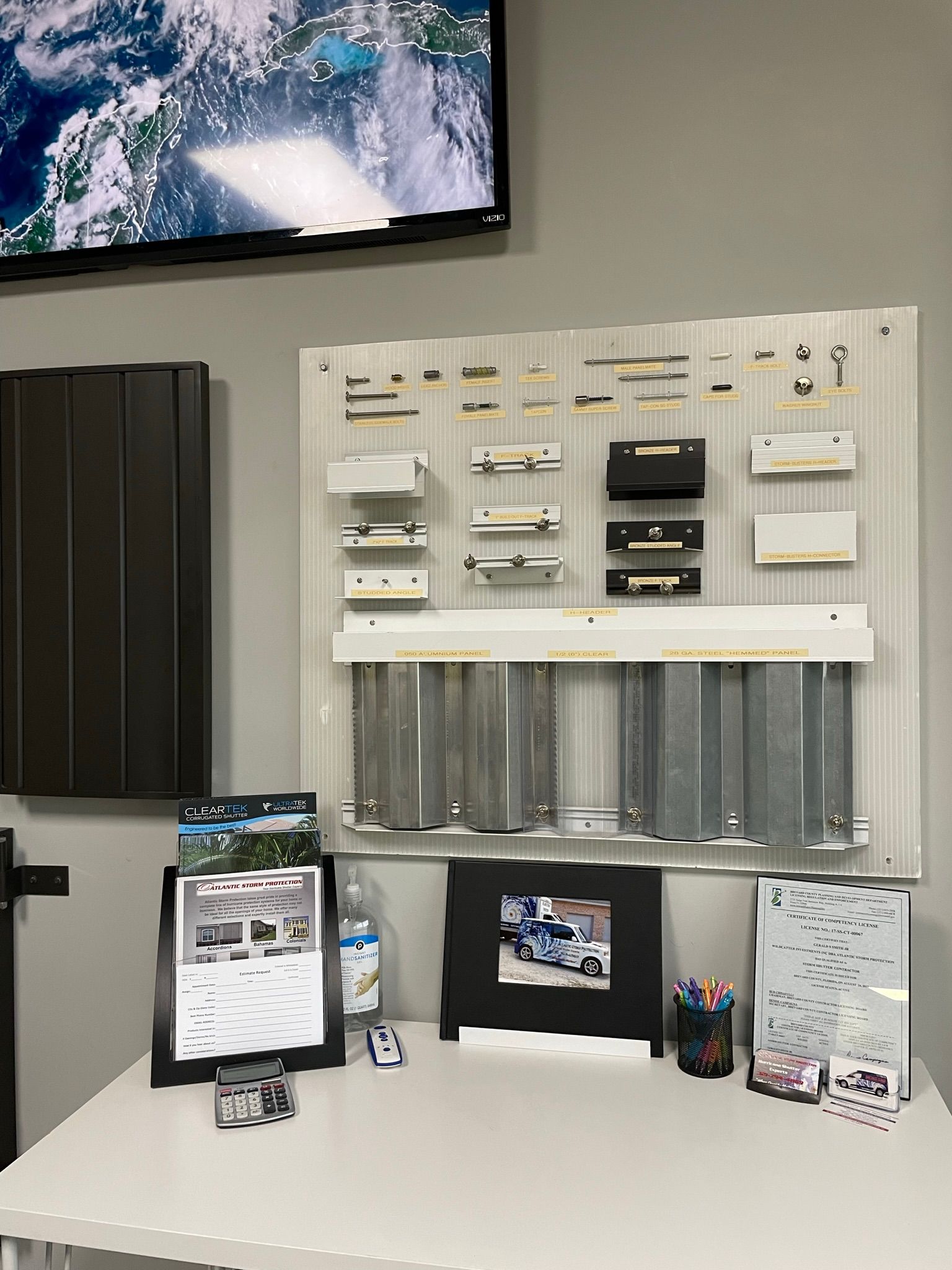 Wall-mounted window blind display with samples, charts, and a TV screen above in a showroom