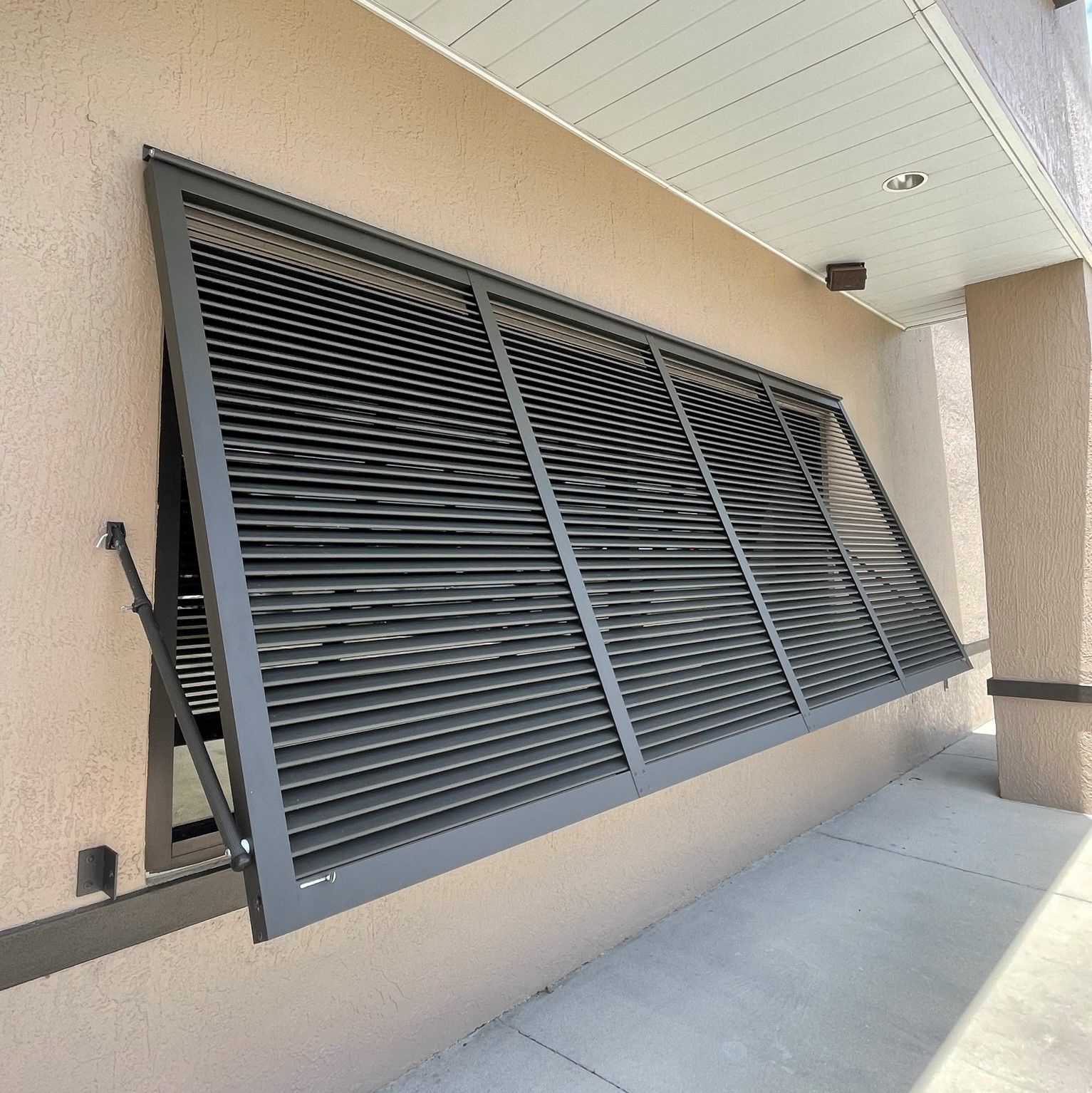 Tilted black louvered window shutters on a beige building exterior under an overhang.