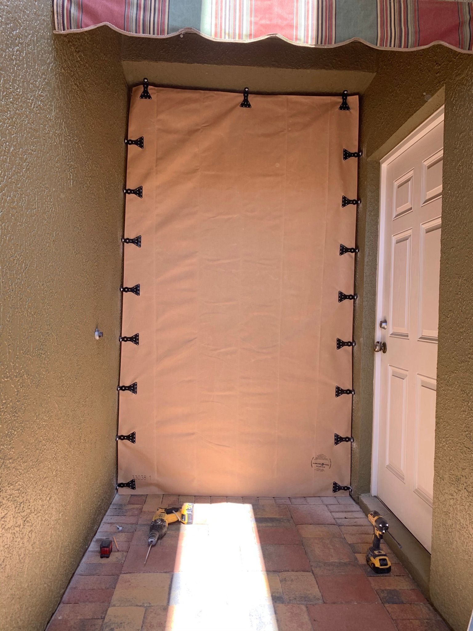 Covered patio with a tan privacy screen stretched between walls, lit by sunlight on the floor.