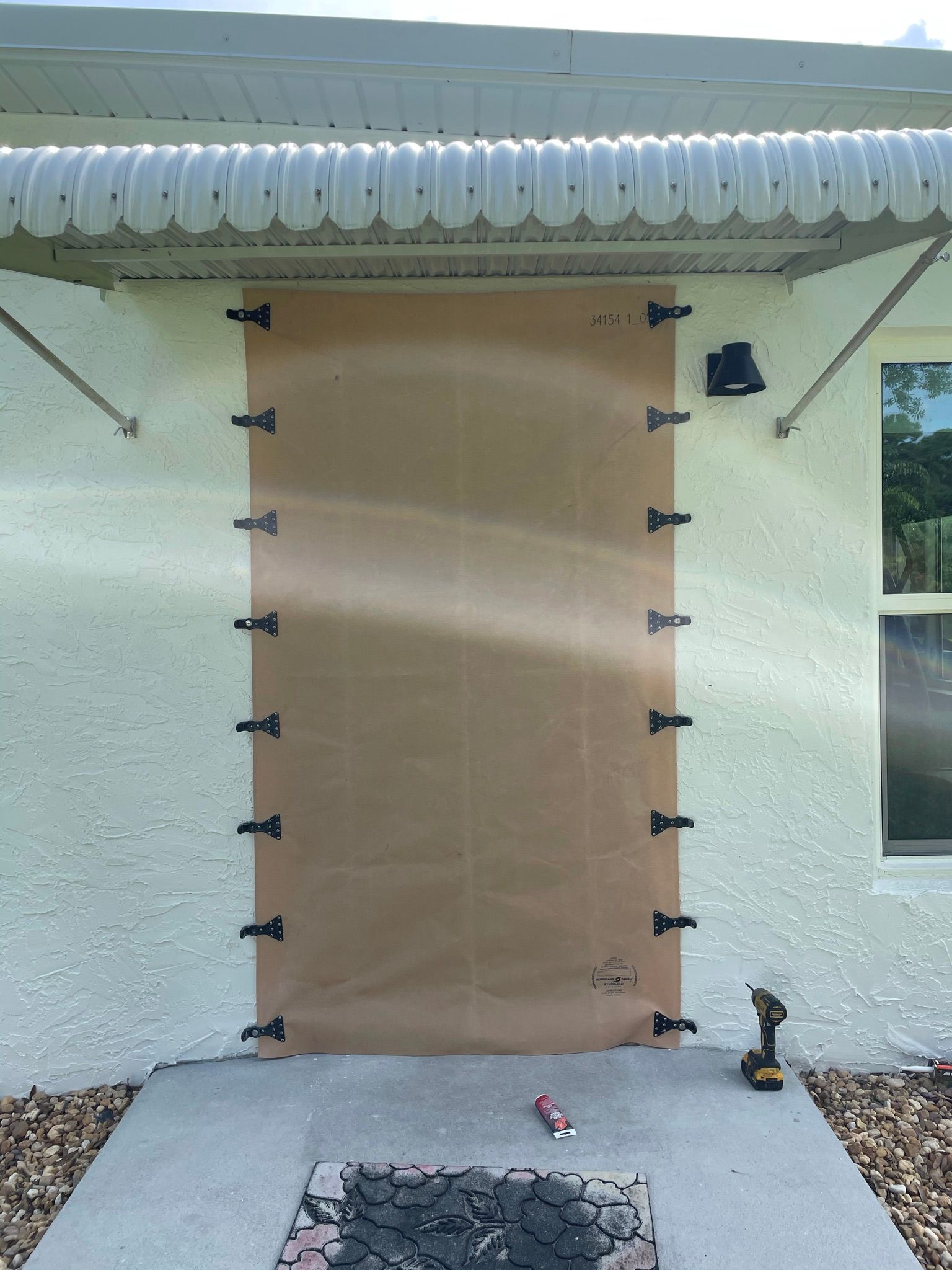 Covered doorway on a stucco house with taped brown paper over the opening, concrete patio, and a cat at right.