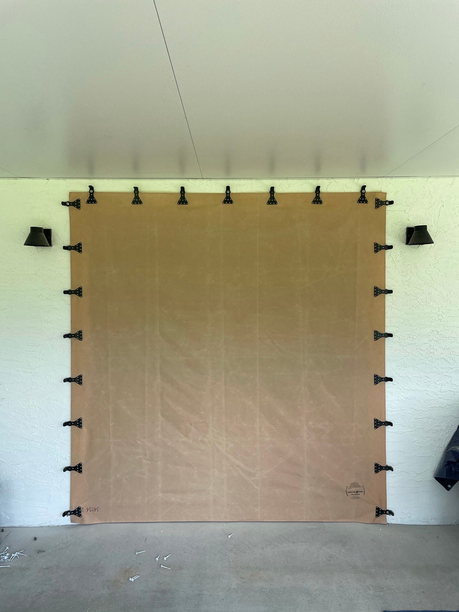Brown board taped to a wall in a garage-like room, with small black clips along the edges.