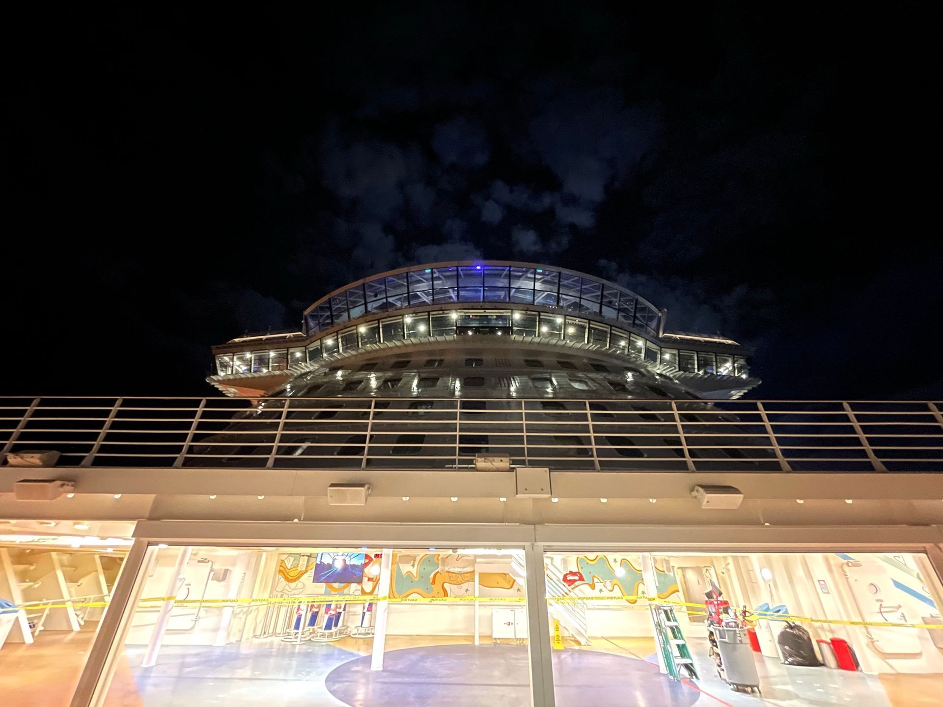 Night view of a glass-fronted building with bright interior lights and a blue-lit roof against a dark sky