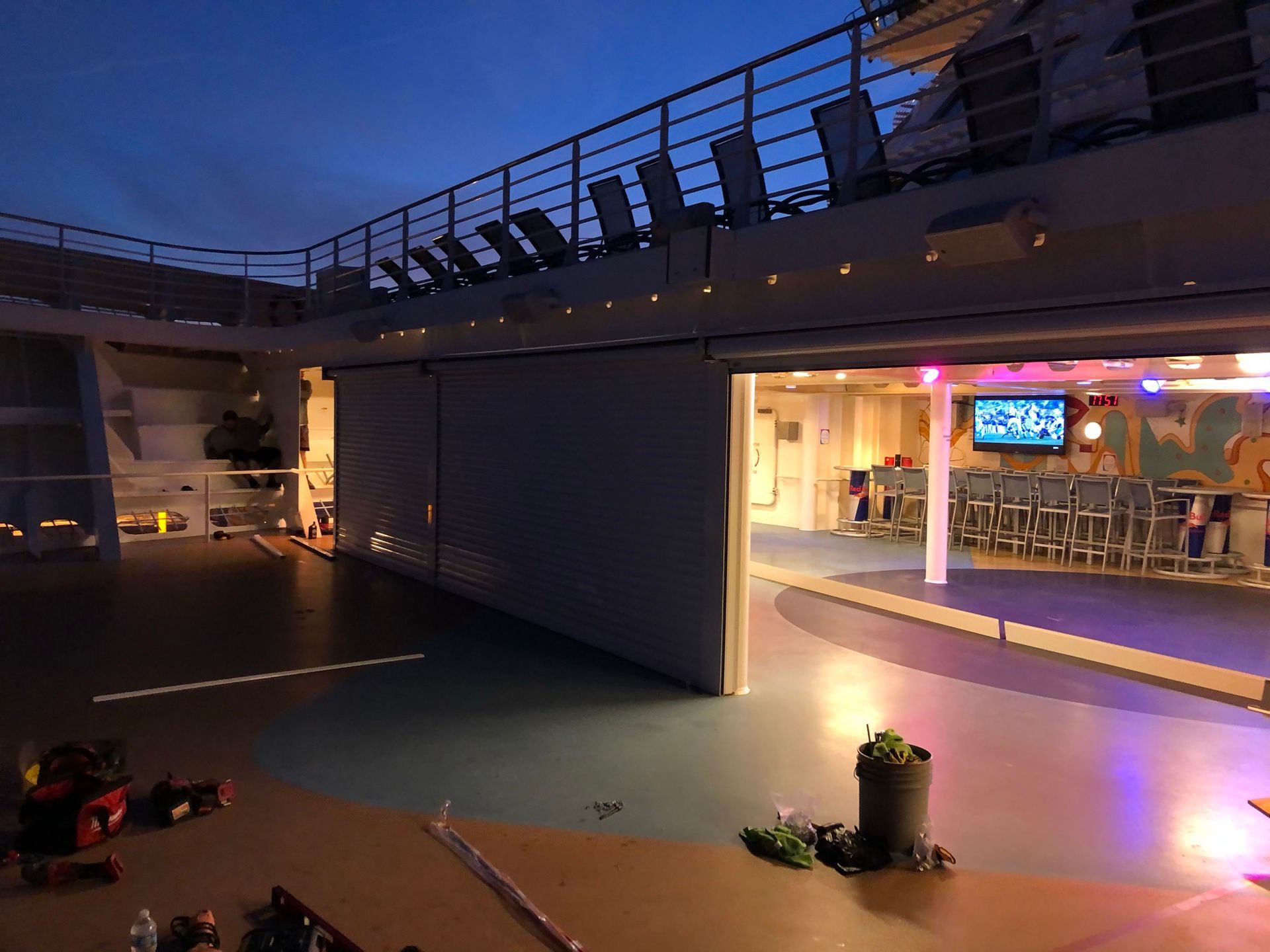 Open-air rooftop lounge at dusk with illuminated bar, tables, and railing under a purple-blue sky
