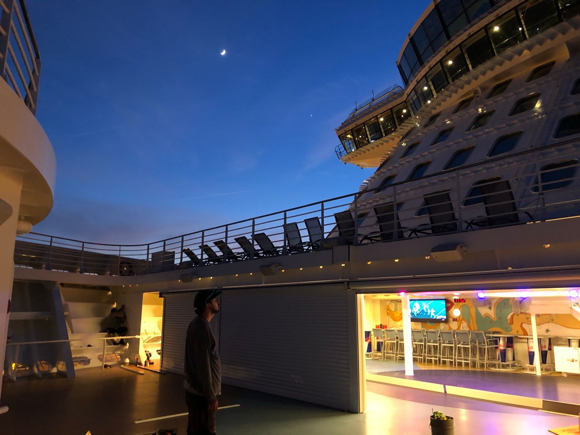 Nighttime deck of a cruise ship, with a person standing beneath blue twilight and lit windows.