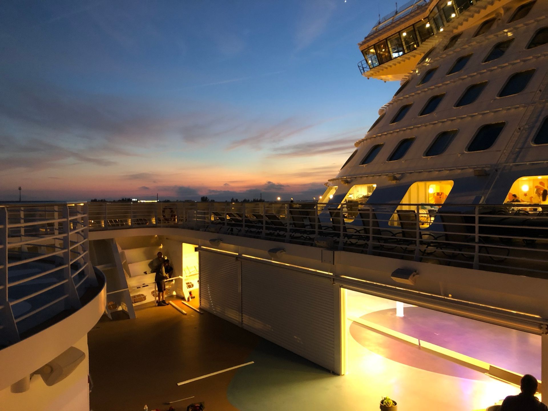 Sunset view of a ship deck with lit windows and railings on a cruise ship