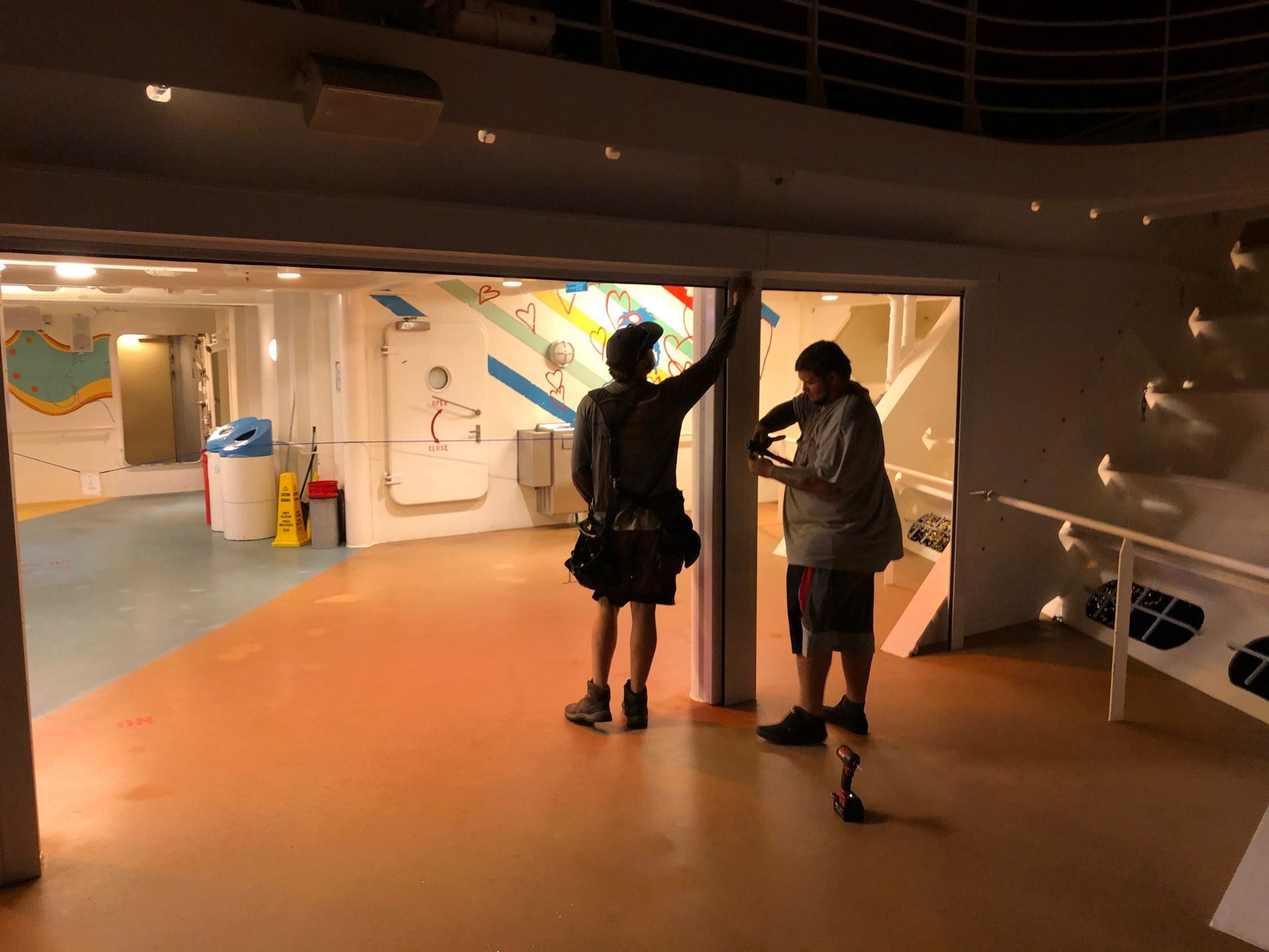 Two people stand in a dim exhibit hall, one reaching up toward a wall display.